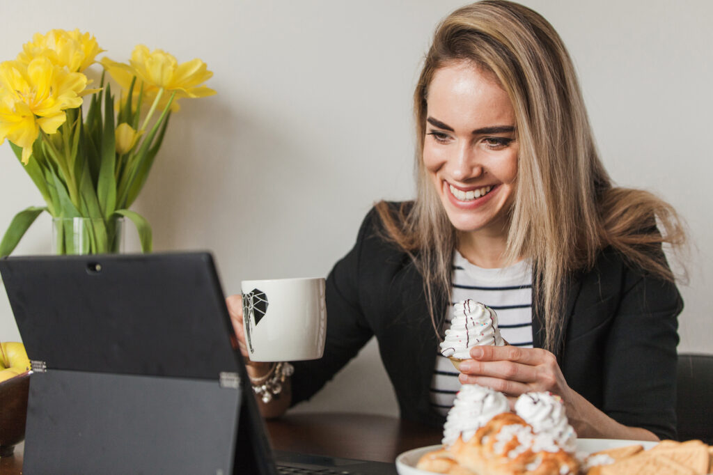 An influencer using live commerce to promote a product. She is holding a cup and a cupcake. 